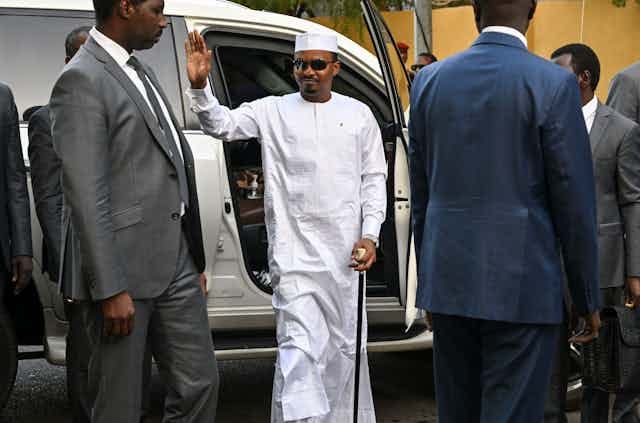 Man wearing white traditional dress alights from a vehicle surrounded by men wearing suits Man wearing white traditional dress alights from a vehicle surrounded by men wearing suits