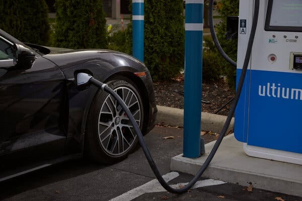A black car is hooked up to an electric vehicle charging station. 