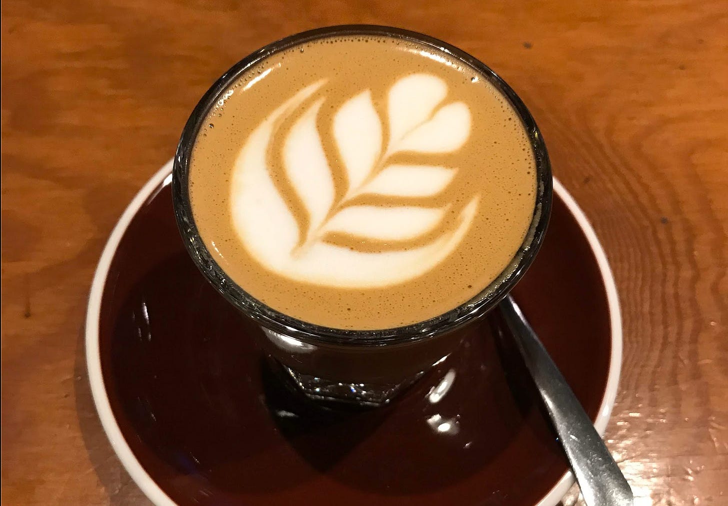 a caffe macchiato in a glass on a wooden table in a coffee shop. a caffe macchiato in a glass on a wooden table in a coffee shop.