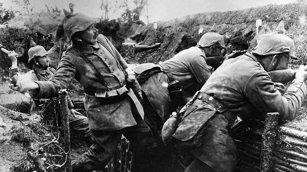 Several men in a trench, one is about to throw a grenade, while others are aiming their rifles
