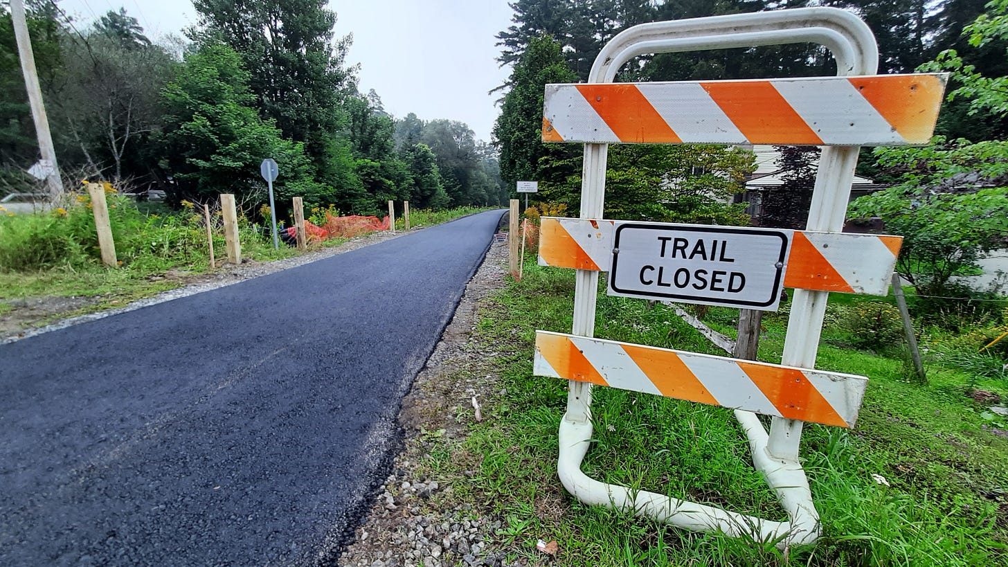 The Adirondack Rail Trail in Saranac Lake is seen with fresh blacktop laid on it, with a Trail Closed sign next to the fresh pavement. The trail is closed while under construction The Adirondack Rail Trail in Saranac Lake is seen with fresh blacktop laid on it, with a Trail Closed sign next to the fresh pavement. The trail is closed while under construction