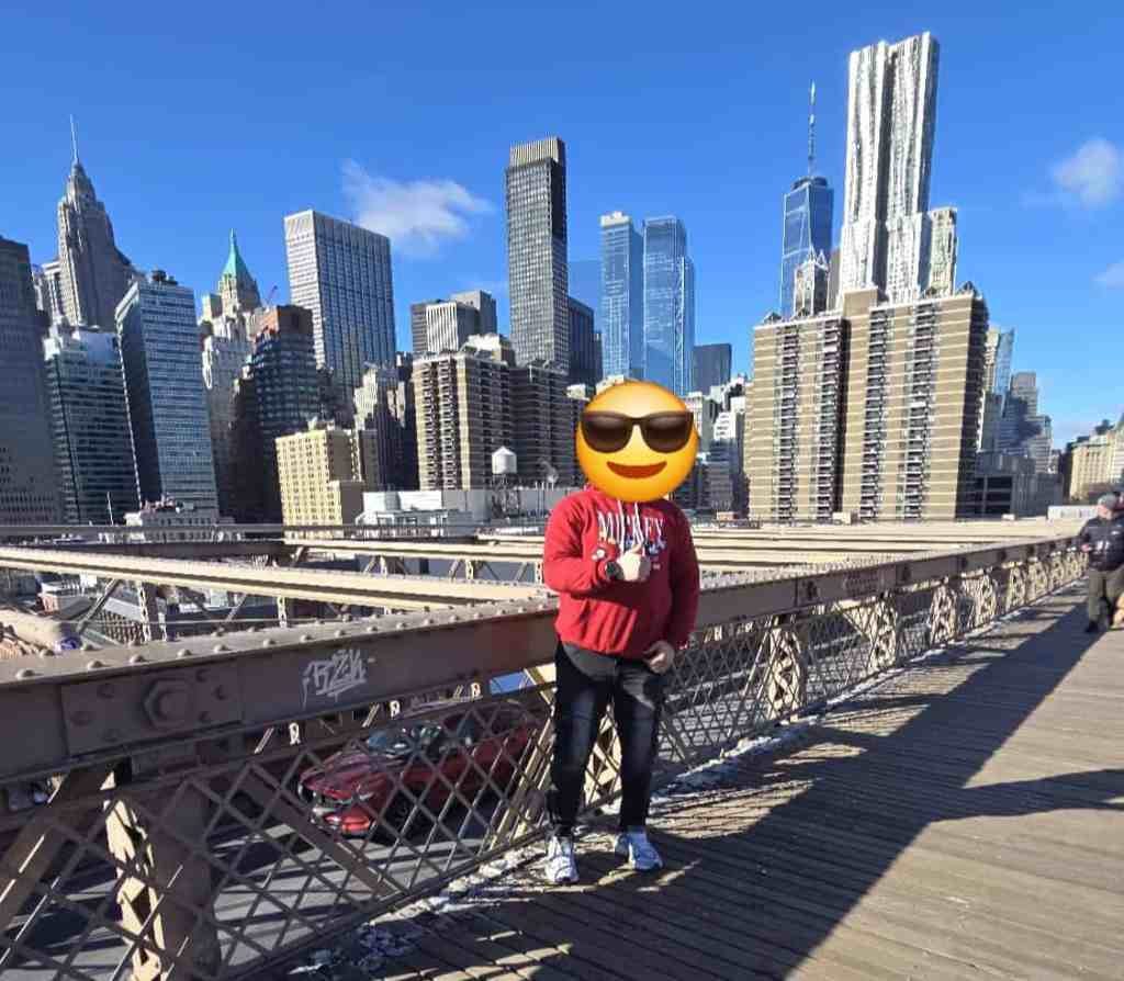 Figure on Brooklyn Bridge with face covered by emoji wearing sunglasses