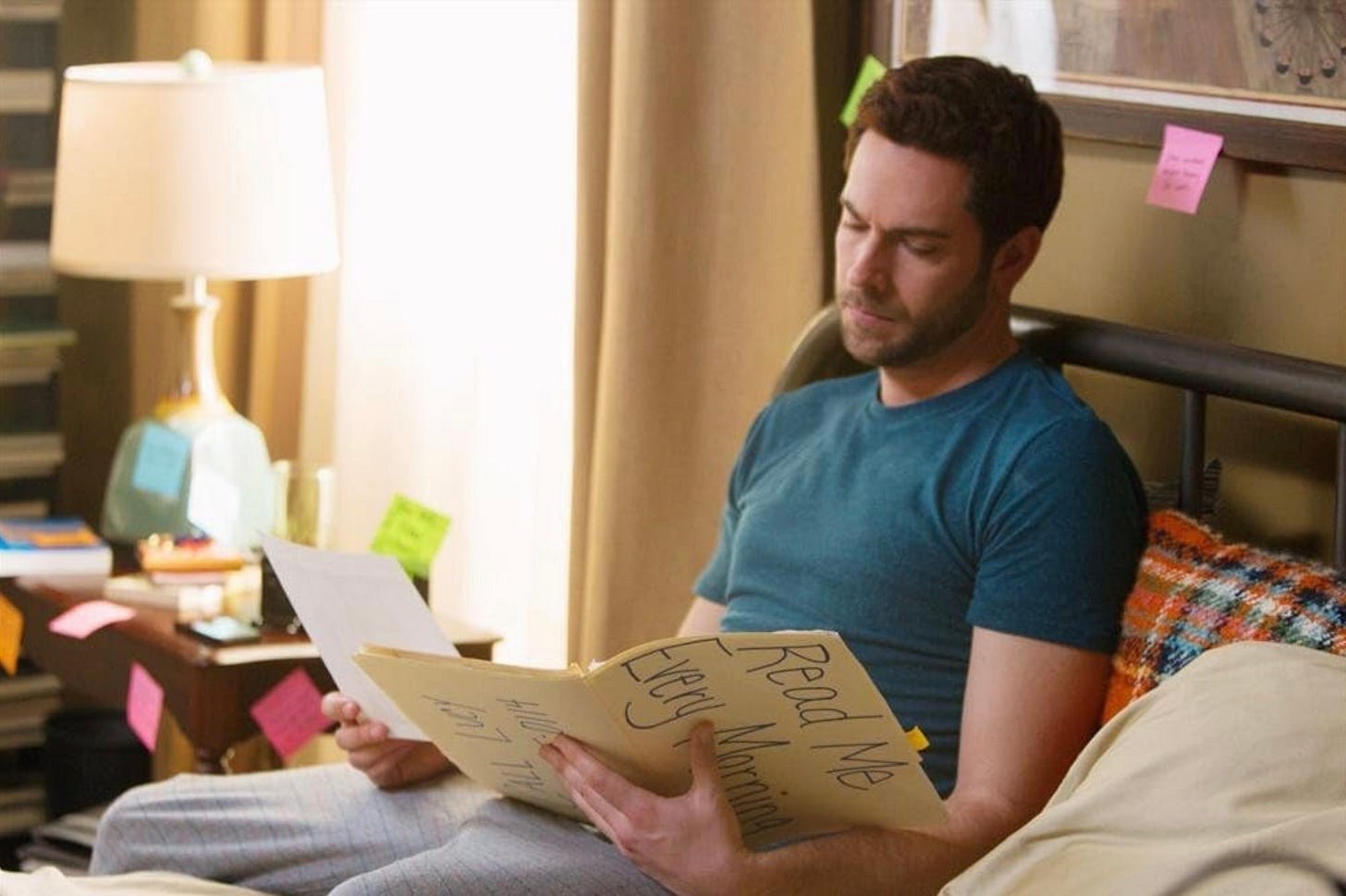 Movie still from _Remember Sunday_ (2013): Gus (Zachary Levi) sits on his bed in the early morning reading looking at a big manila folder labeled “Read Me Every Morning”. (c) 2013 Hallmark
