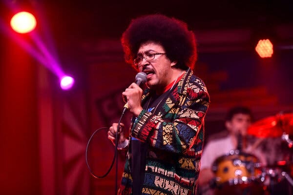 Cola Boyy sings into a microphone on a red-lit stage.