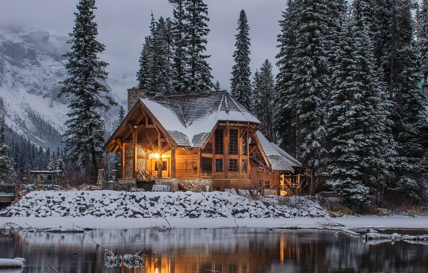 wooden house near pine trees and pond coated with snow during daytime