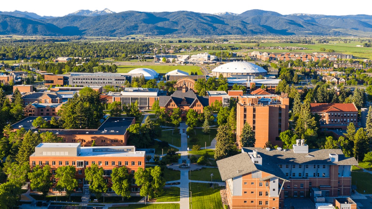 An aerial view of the Montana State University campus set against a backdrop of rolling hills and distant mountains.