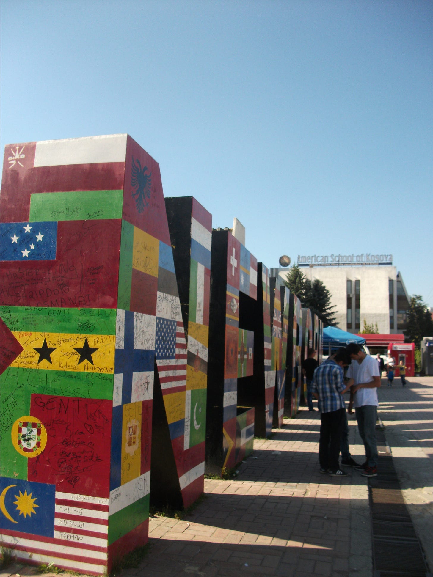 A 12 foot monument reading NEWBORN covered in the flags of the world on a sunny day A 12 foot monument reading NEWBORN covered in the flags of the world on a sunny day