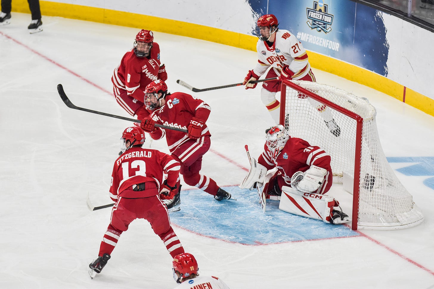 Wisconsin Badgers captain Ben Dexheimer with stick above head after firing puck down ice away from goal.