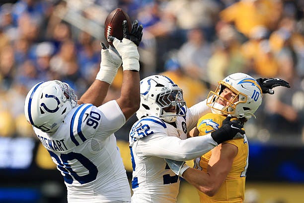 Grover Stewart of the Indianapolis Colts intercepts a pass while Samson Ebukam of the Indianapolis Colts hits Justin Herbert of the Los Angeles...
