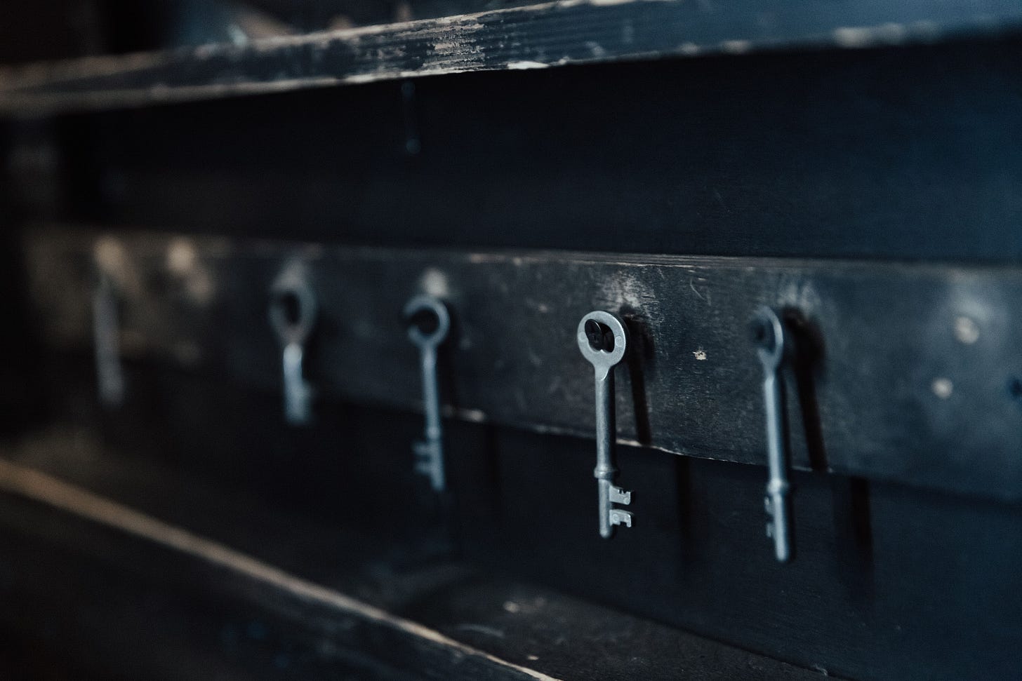A row of old keys hanging separately along a dark rail, the article's image for authority handed out and never coordinated. A row of old keys hanging separately along a dark rail, the article's image for authority handed out and never coordinated.