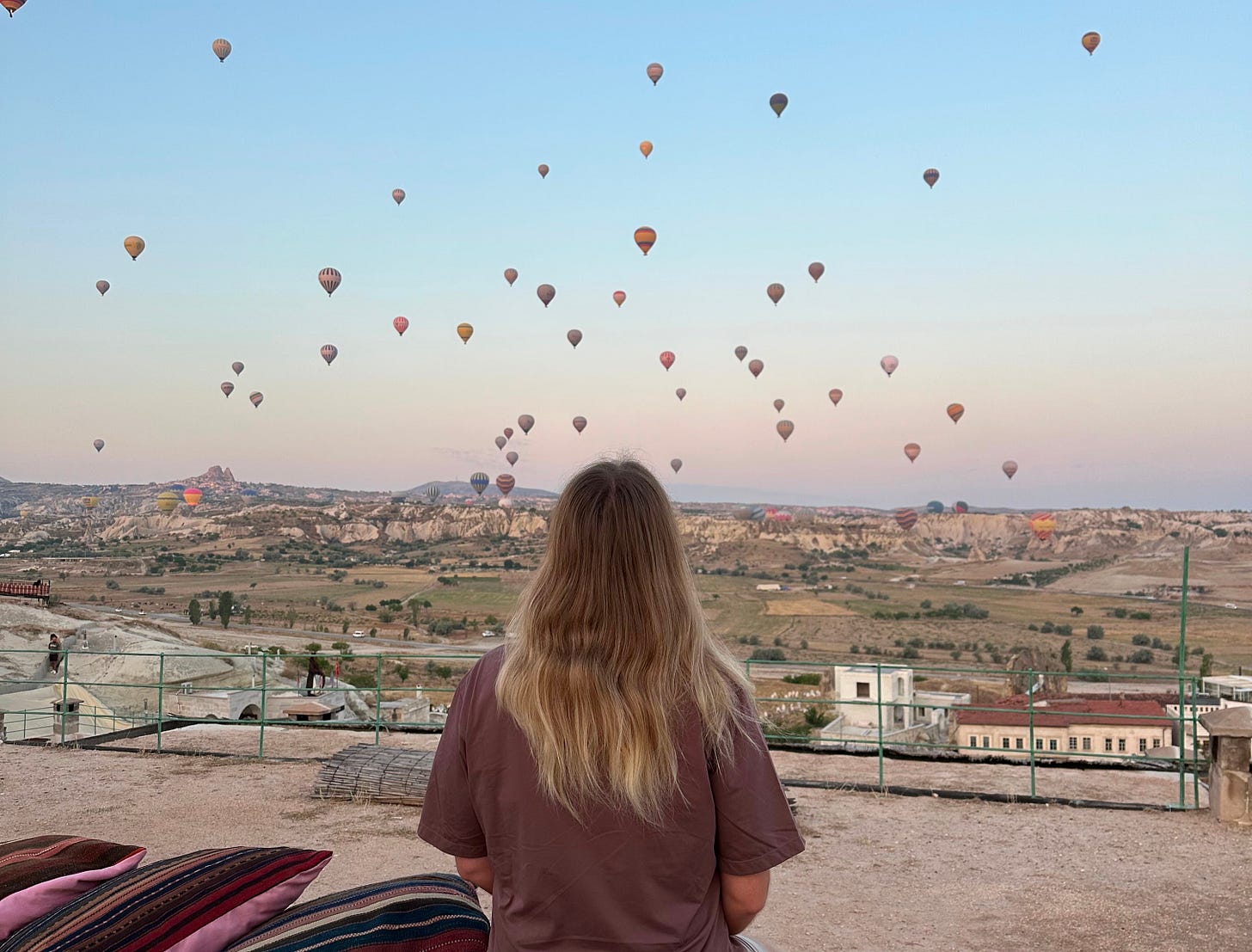 A person with their back to the camera, watching dozens of hot air balloons take flight. 