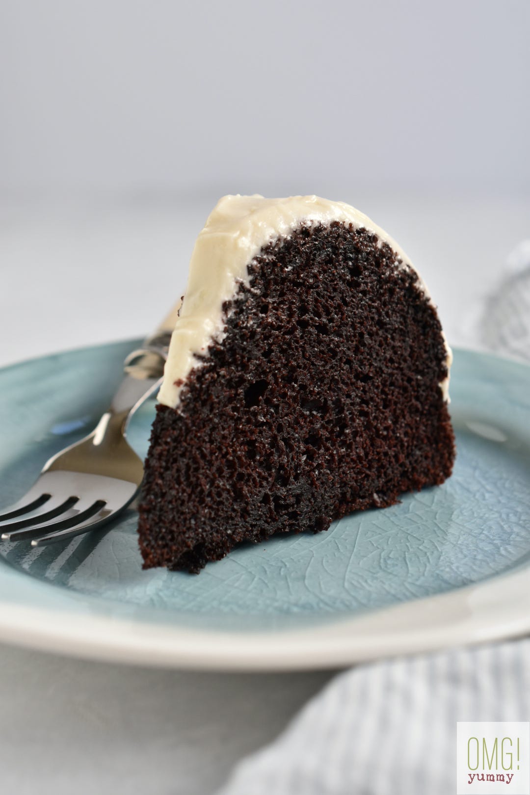 Slice of chocolate cake with cream cheese frosting on a blue plate.
