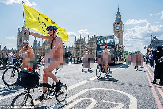 Nude cyclists, blurred with mosaic blocks, ride near Buckingham Palace, past Big Ben on bikes. One holds a large yellow flag with a smiley face on it. 