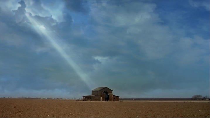 Wide shot of an isolated barn in an empty field with a single beam of light breaking through stormy clouds above.
