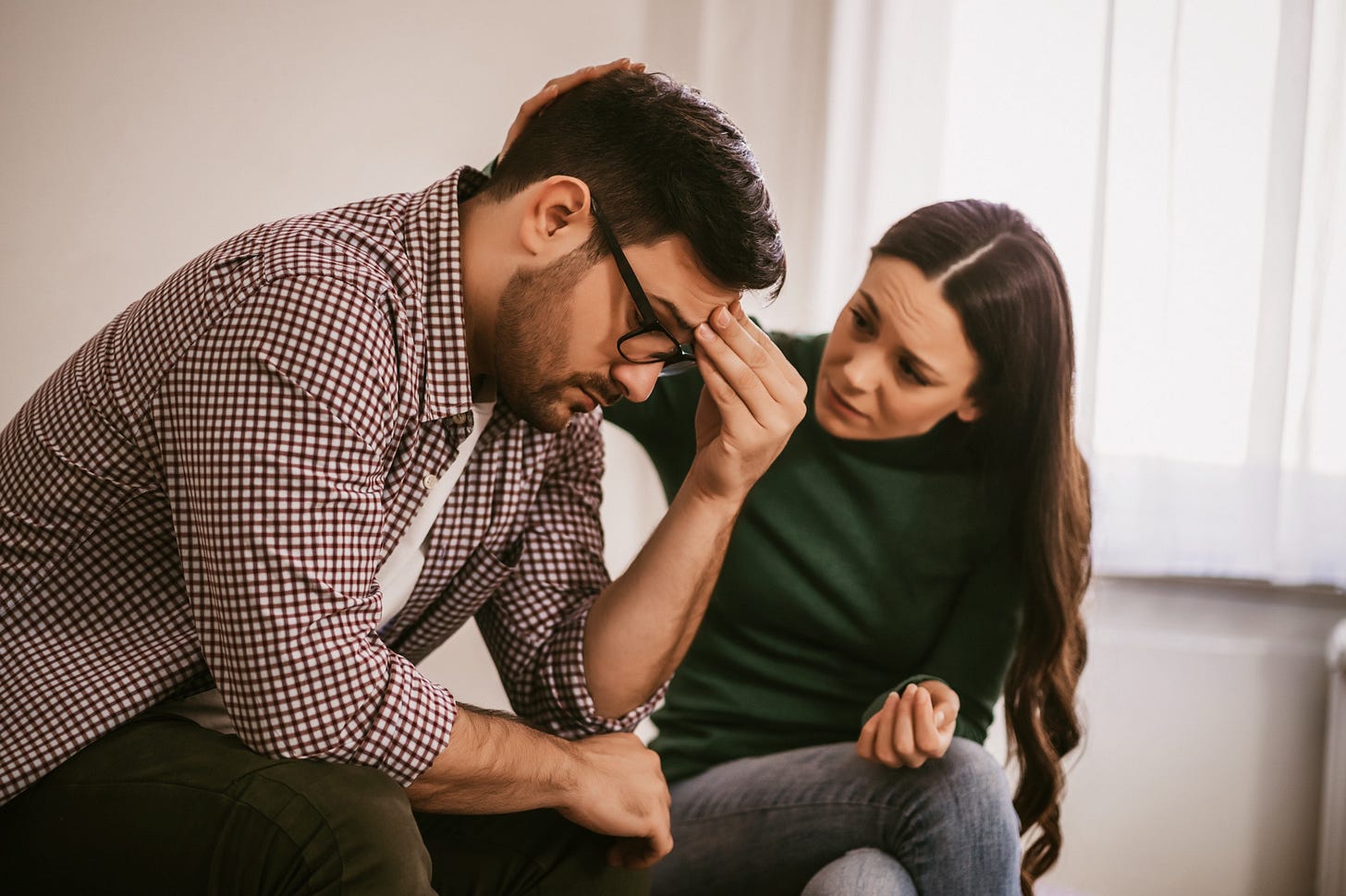 A woman consoles her male partner while sitting next to him. Her hand rests gently on his head.
