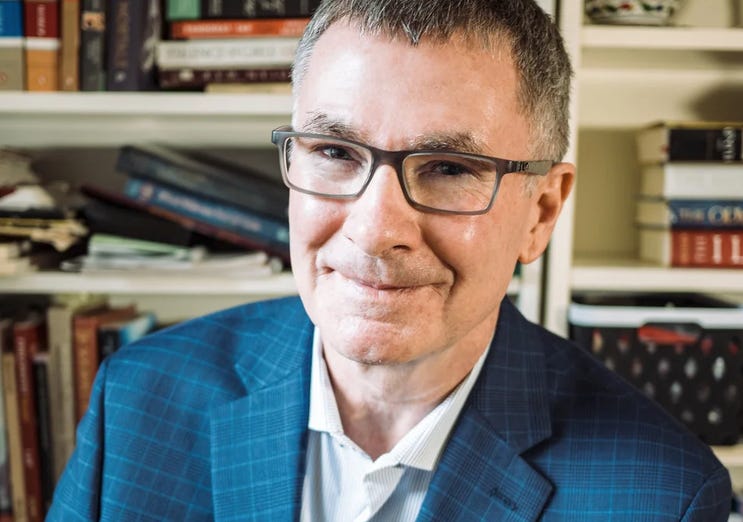 Jeff Wright smiling in a blue plaid blazer, seated in front of bookshelves lined with books. Jeff Wright smiling in a blue plaid blazer, seated in front of bookshelves lined with books.