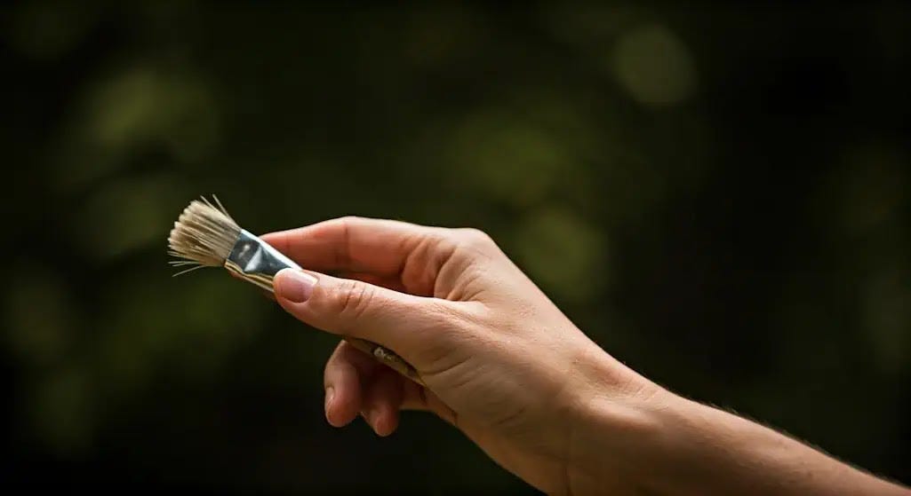 A close-up image depicts a woman's hand gripping a paintbrush, revealing a subtle tremor that illustrates the symptoms of fibromyalgia.