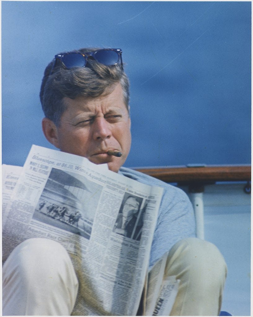 John F. Kennedy reading while smoking a cigar.