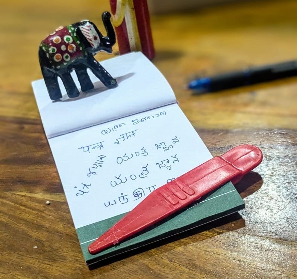 Handwriting in several Indian scripts on a notepad, beside a pen and a pair of Channapatna wooden toys Handwriting in several Indian scripts on a notepad, beside a pen and a pair of Channapatna wooden toys