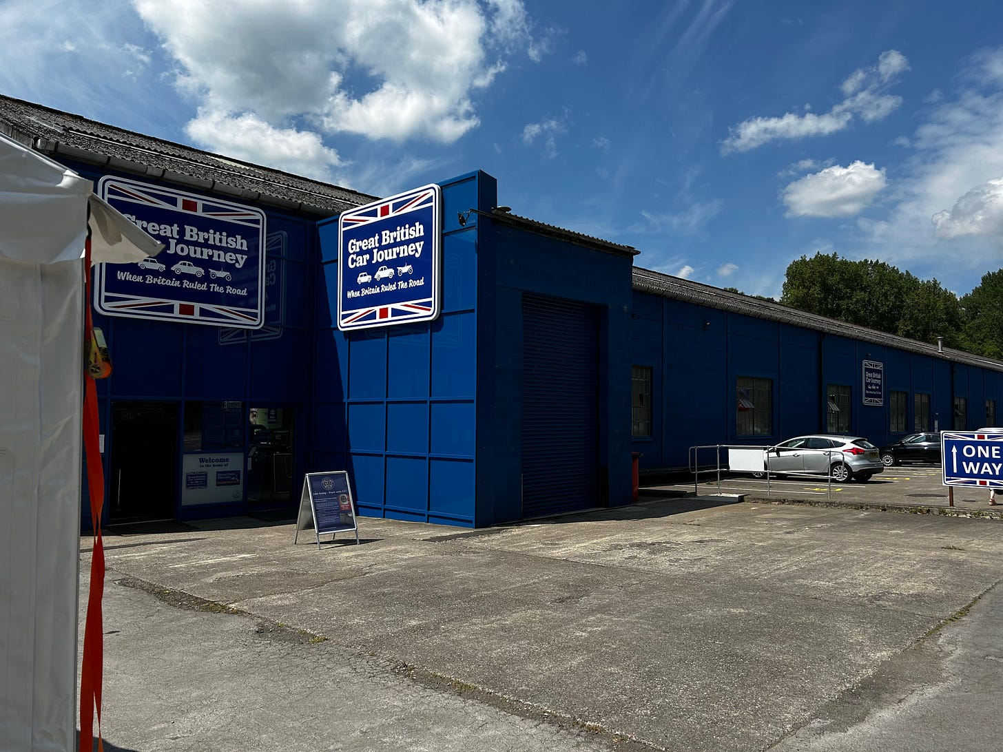 The entrance to The Great British Car Journey. The June sunshine is falling onto the long blue rectangular building. 