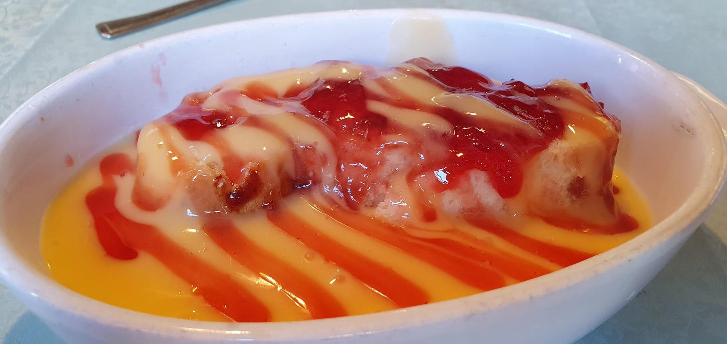 A white china bowl is shown holding a pool of thick custard and a serving of raspberry jam, steam slowly rises.