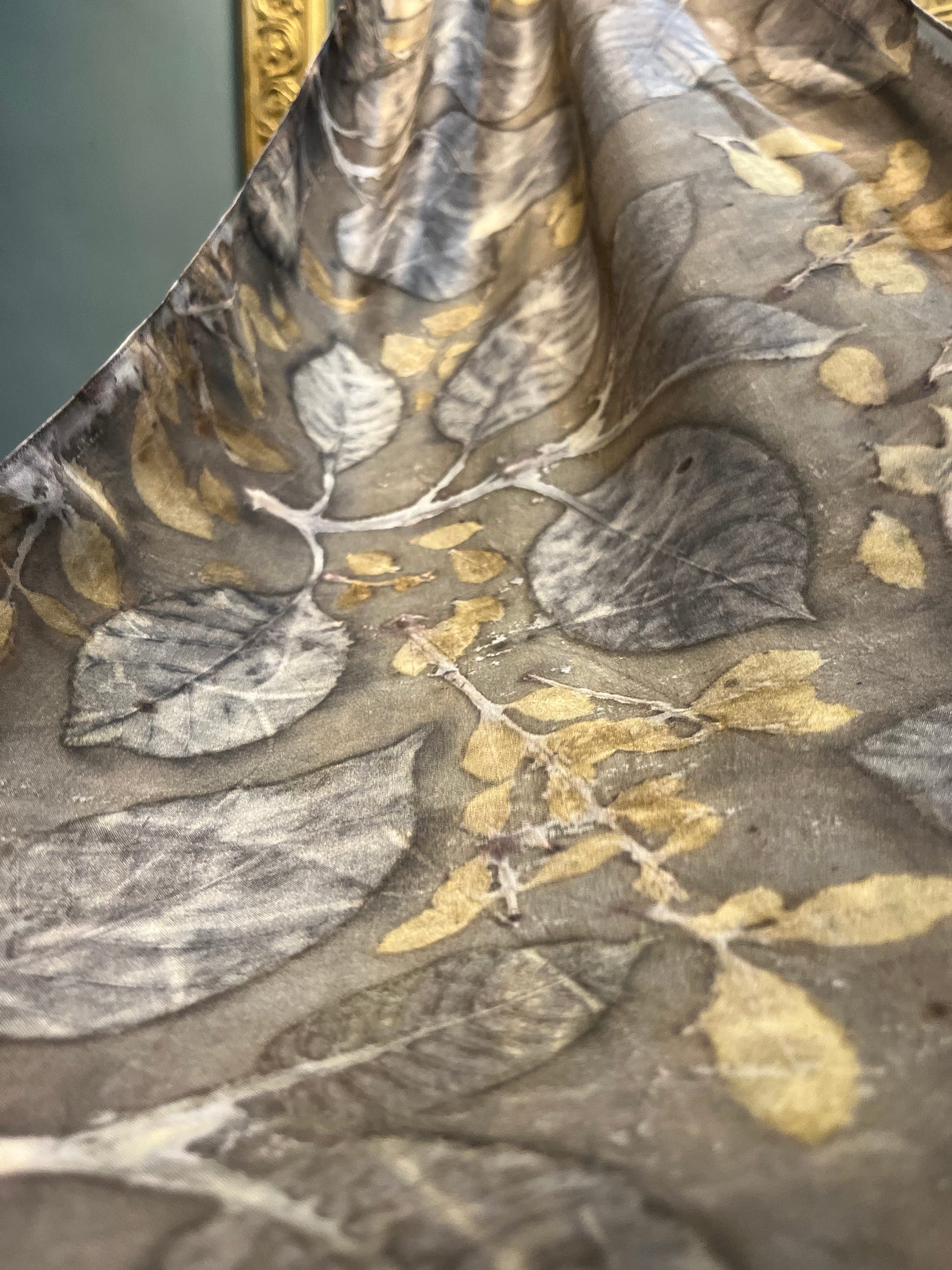 Close-up of eco-printed fabric showing soft gray tones with pale yellow leaf shapes.