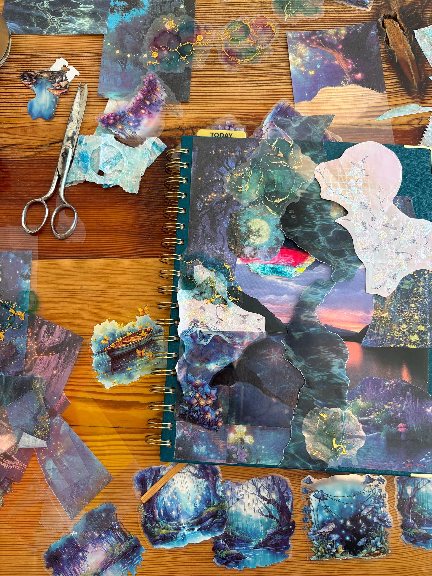 A wooden desk covered in twilight forest ephemera like stickers and paper with a journal to one side and scissors to the other