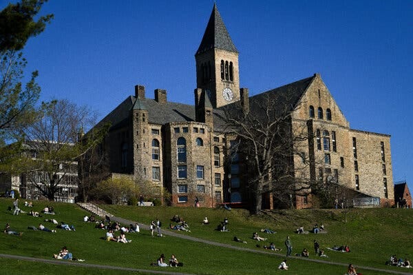 Students sit on a hill below a large academic building.
