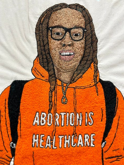 1 - 2) Brittney Griner's portrait is seen fron the front view. In it, she is wearing an orange hoodie that says 'Abortion is healthcare'. She has dreads, some of which are tucked into her hoddie, and she is wearing white shorts, and white leggings underneath. She has on black sneakers, and black backpack straps on her shoulders. She also has thin-framed black square glasses on. 3) The verso side of the embroidery is seen with different messages attached, and messy stringwork. 4) A close-up of the verso side shows some of the texts strings on black fabric like 'Brittney Griner', 'Two-time olympic gold medalist', and 'NCAA Final Four'. 5) The front of the portrait is seen at a gallery, surrounded by two other works on eithe side. It's sitting on a tall white pedestal. The gallery's walls are white, with black stone flooring.