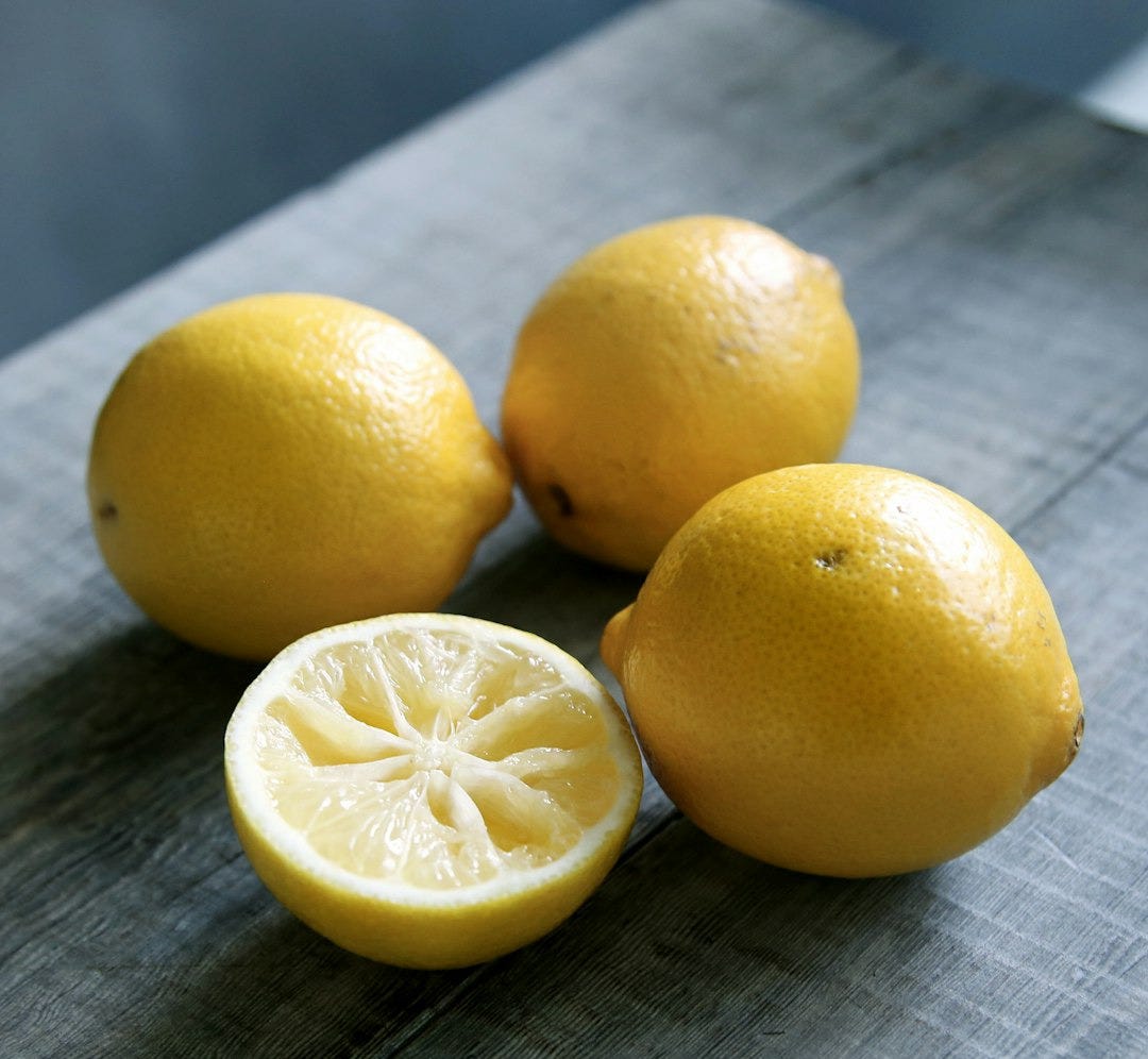 three yellow lemons beside sliced lemon placed on gray wooden surface three yellow lemons beside sliced lemon placed on gray wooden surface