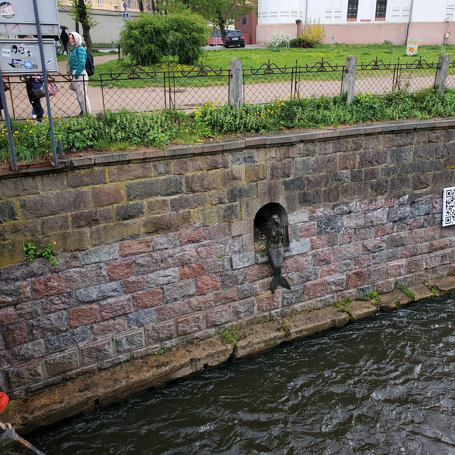 A small mermaid statue set in an alcove in a stone wall along the river.