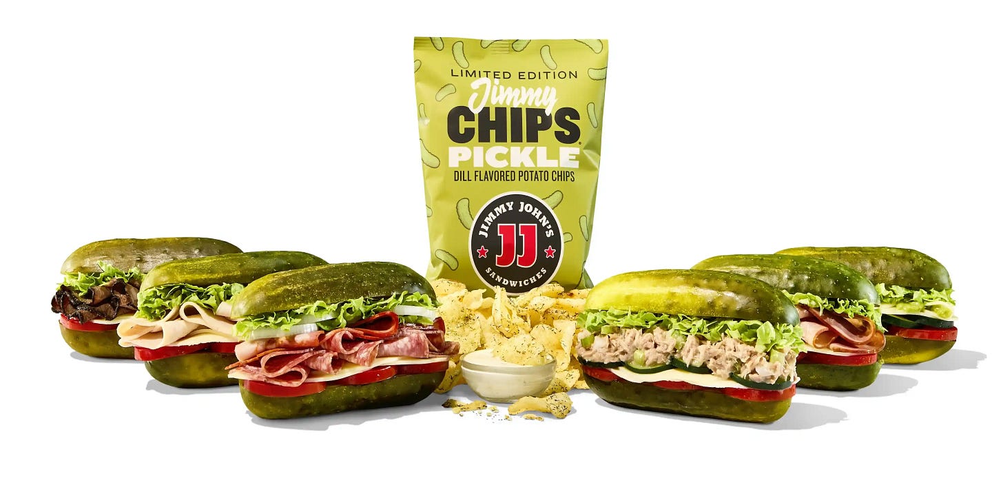 Six large pickles with meat in the center in sandwich-shapes with a bag of Jimmy John's pickle chips in the background