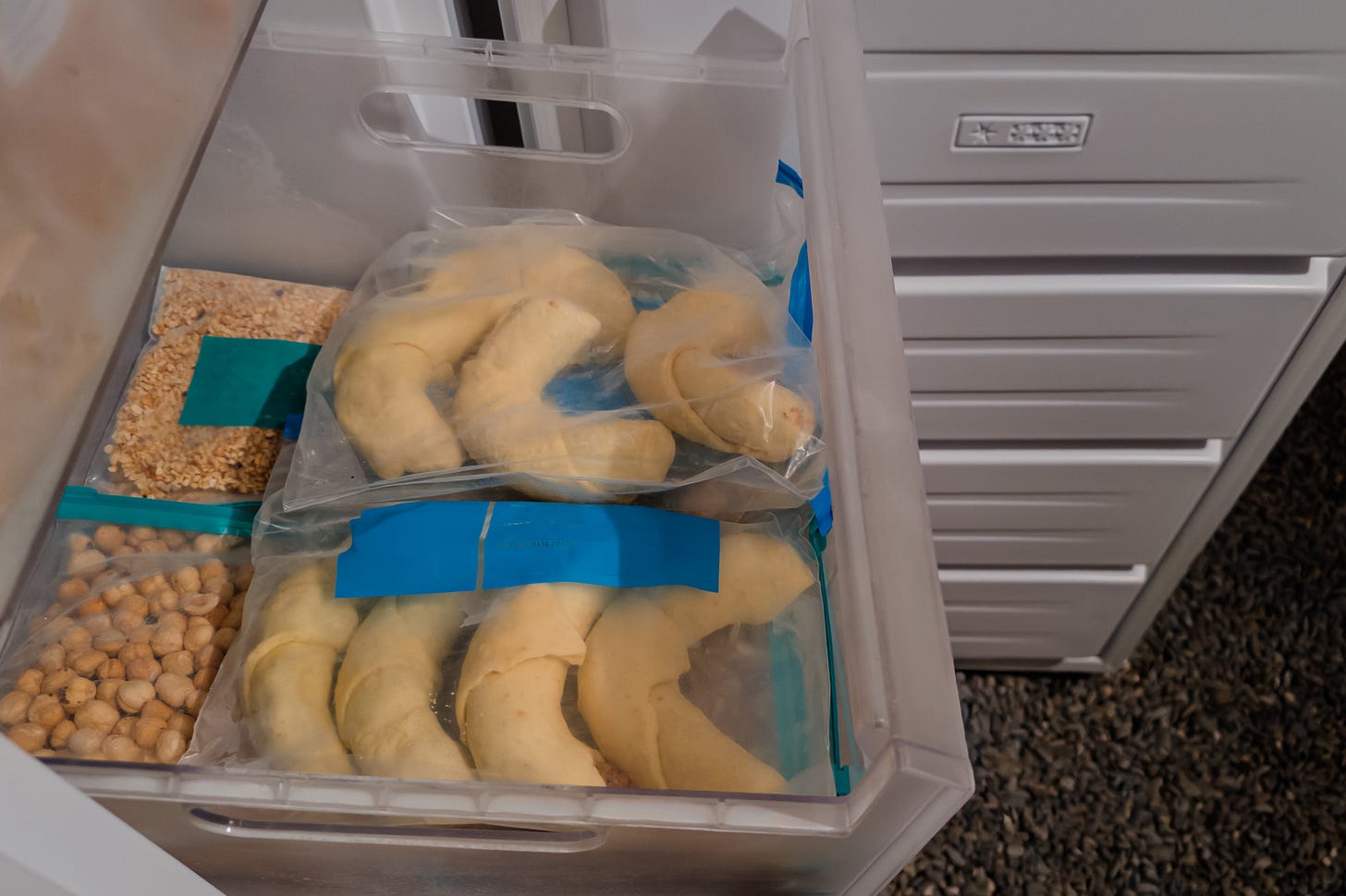 Geöffneter Tiefkühler mit einer Schublade, in der portionierte Haselnüsse und Baumnüsse in Gefrierbeuteln lagern. Darüber liegen zwei Beutel ungebackene Nussgipfel auch in Gefrierbeuteln. Geöffneter Tiefkühler mit einer Schublade, in der portionierte Haselnüsse und Baumnüsse in Gefrierbeuteln lagern. Darüber liegen zwei Beutel ungebackene Nussgipfel auch in Gefrierbeuteln.