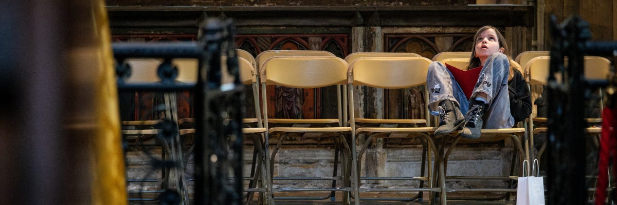 A young girl sits in a cathedral alone, looking up at the ceiling in awe