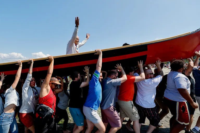 Skipper Wayne Price, a master carver from the Tlingit people, holds up his arms as he and his dugout canoe, North Tide, are carried up the beach by volunteers. (Jennifer Buchanan / The Seattle Times)