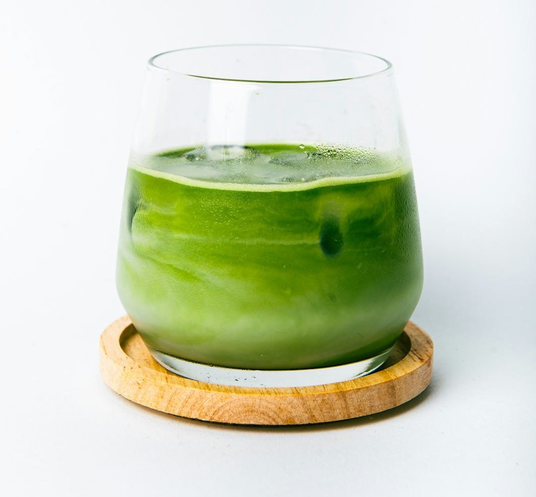 a green liquid in a glass with a wooden coaster