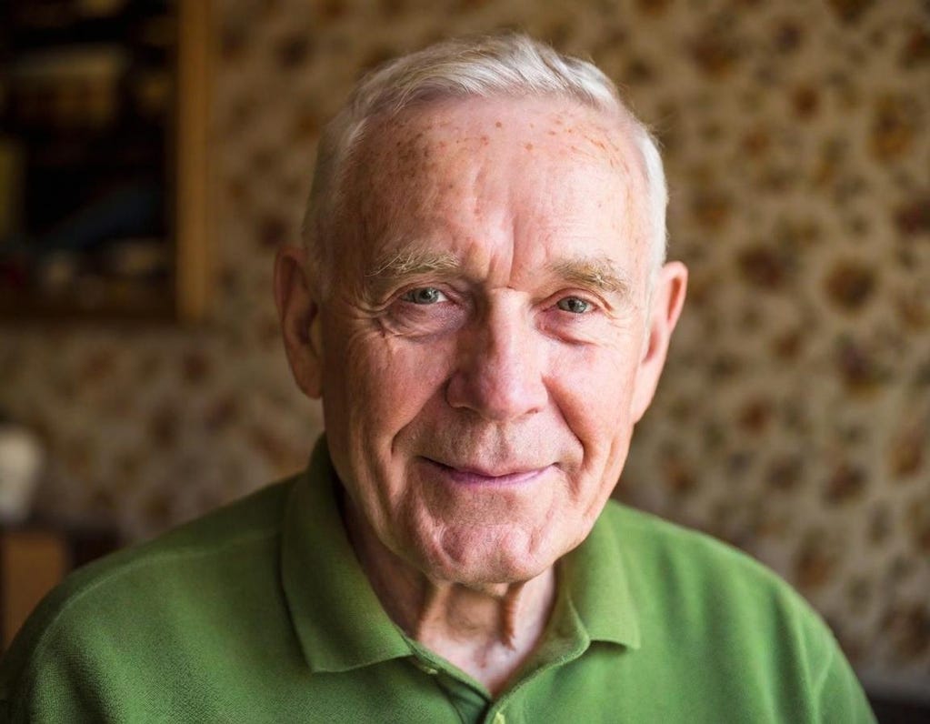 Portrait of white 87-year-old man without glasses. He’s wearing a green shirt and a faint smile.