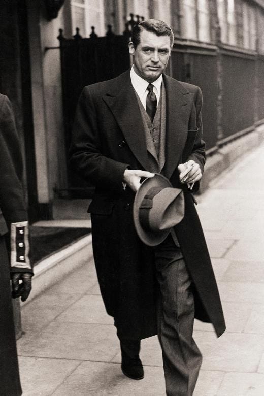 This may contain: a man in a suit and tie walking down the street with a hat on his shoulder