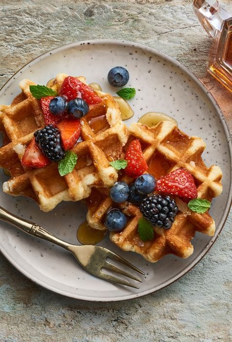 This may contain: waffles with fruit and syrup on a plate