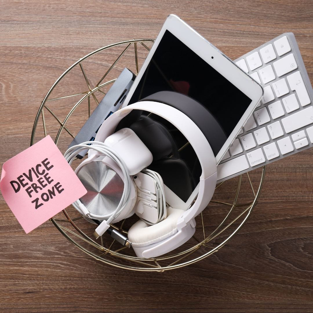 a wire trash can with laptop keyboard headphones and other tech items in it with a post-it note that reads device free zone, via Canva