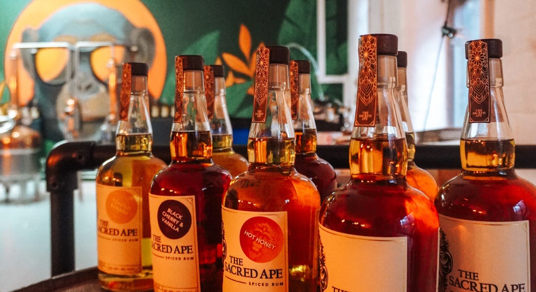 A collection of Sacred Ape rum bottles on a table with an ape mural behind them A collection of Sacred Ape rum bottles on a table with an ape mural behind them