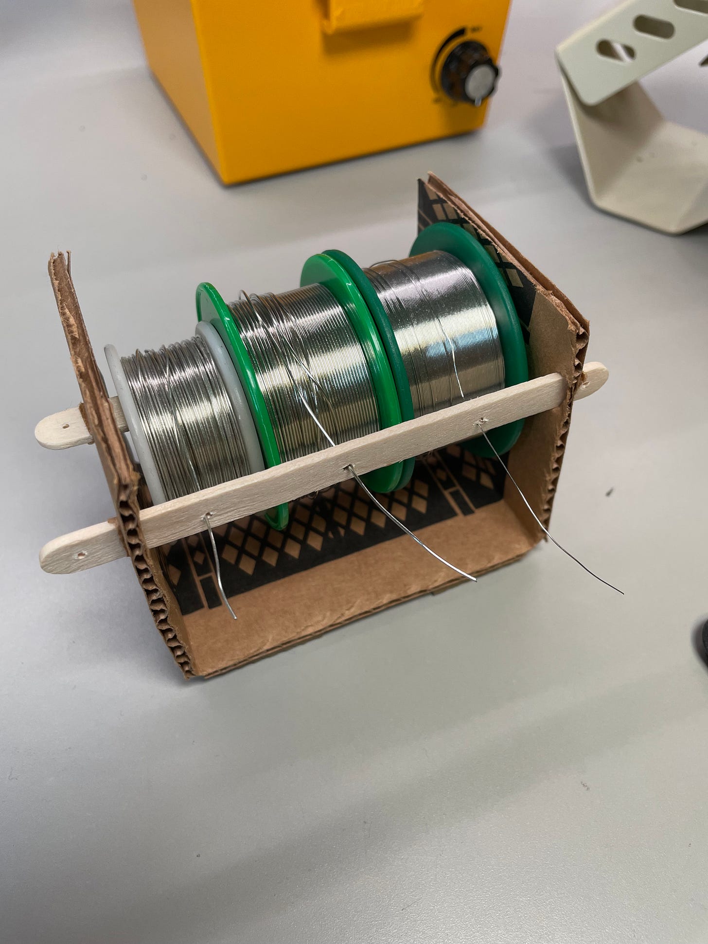 two popsicle sticks shoved through slits in folded cardboard, holding solder spools