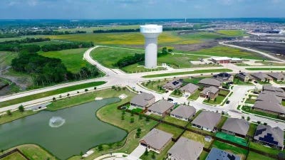Aerial of white water tower next to new single-family homes on small lake in Texas.