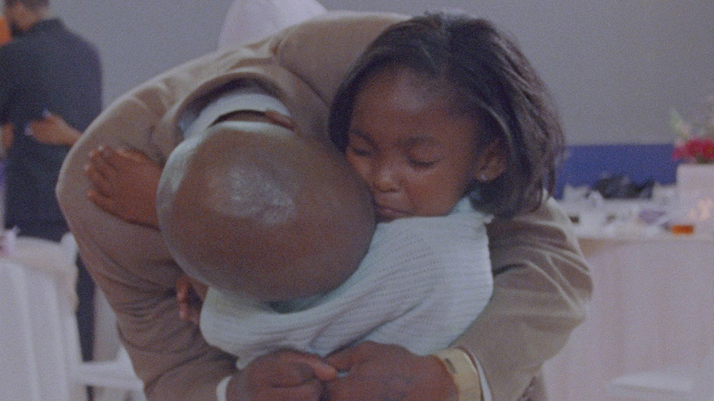 bald incarcerated dad in suit hugging his five year old; he's bending down and his face is hidden; her eyes are closed