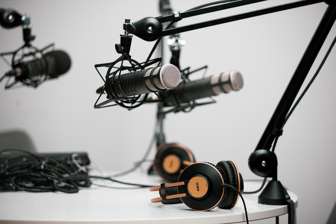 Three podcasting microphones on boom arms at a teble with headphones in shot. Three podcasting microphones on boom arms at a teble with headphones in shot.