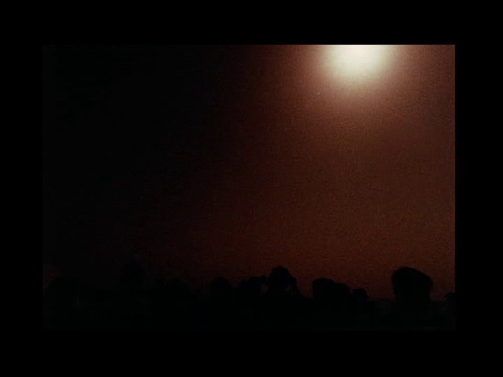 The fourth of four shots from a sequence in Peter Rose's The Man Who Could Not See Far Enough depicting a crowd on a ship watching a solar eclipse. The sky is almost totally dark, the crowd is almost invisible in shadow, and the glare from the sun more or less takes over the focus of the viewer.