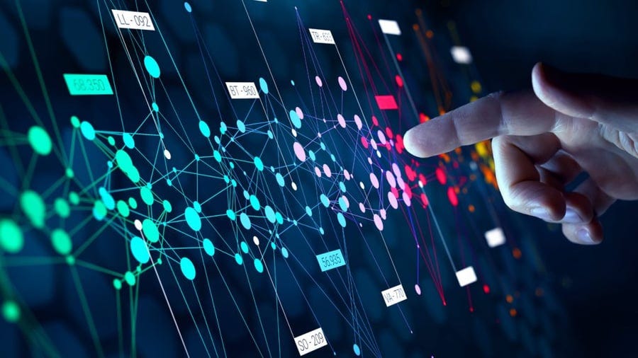 A hand is pointing at a glowing, colorful network of connected nodes and data points on a digital interface. A hand is pointing at a glowing, colorful network of connected nodes and data points on a digital interface.