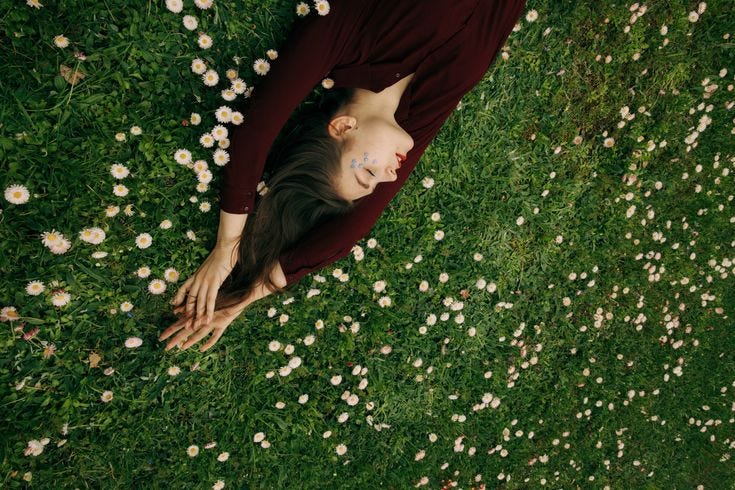 This may contain: a woman laying on top of a lush green field covered in flowers and daisies