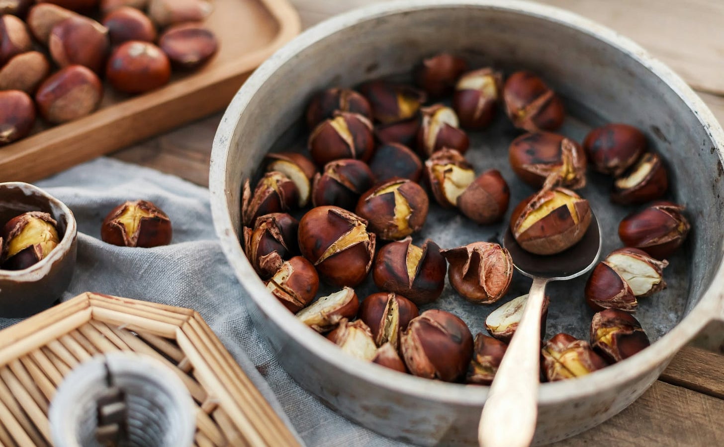 a tin bowl of roasted chestnuts sitting on a wooden table