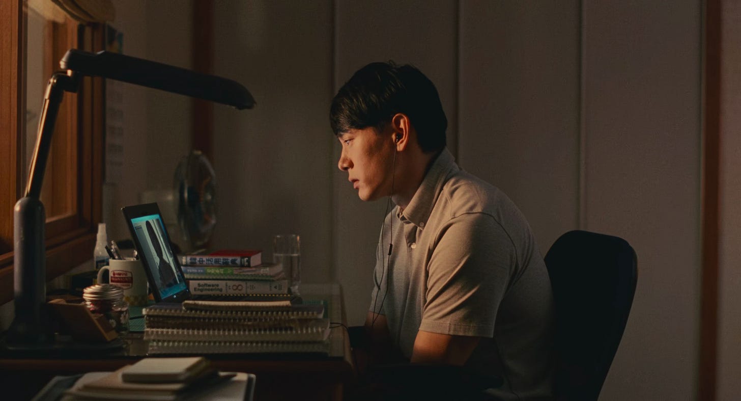 Hae Sung jovem sentado à escrivaninha em seu quarto, visto de perfil, olhando para o computador durante uma chamada de vídeo com Nora, capturando o momento da reconexão virtual após 12 anos separados.